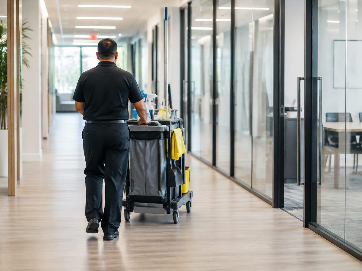 Cleaning professional with a janitorial cart in an office hallway